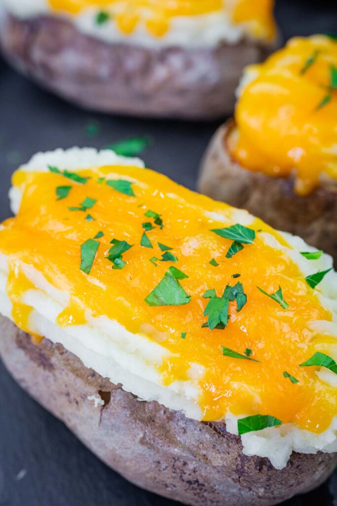 Close-up of Shepherd’s Pie Baked Potatoes topped with melted cheddar cheese and chopped parsley.