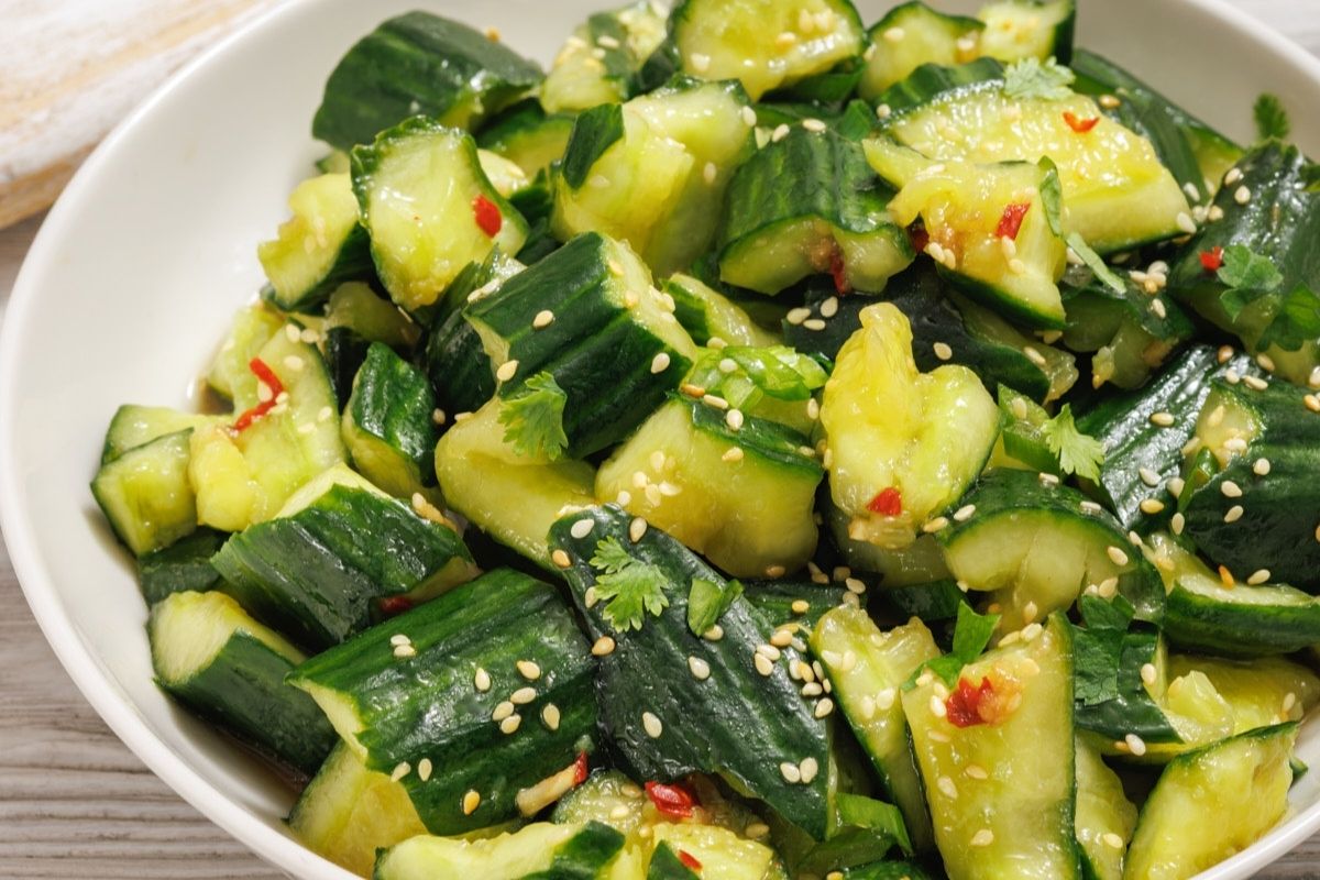 A bowl of smashed cucumber salad with sesame seeds, red chili pieces, and cilantro.