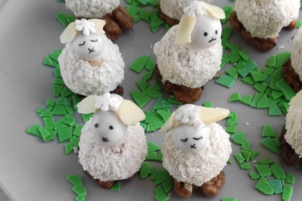 Coconut Easter Bunny Candies with coconut-covered bodies and walnut feet, surrounded by green candy shards on a gray plate.