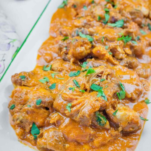 A rectangular plate filled with chicken pieces in an orange curry sauce, garnished with chopped green herbs.