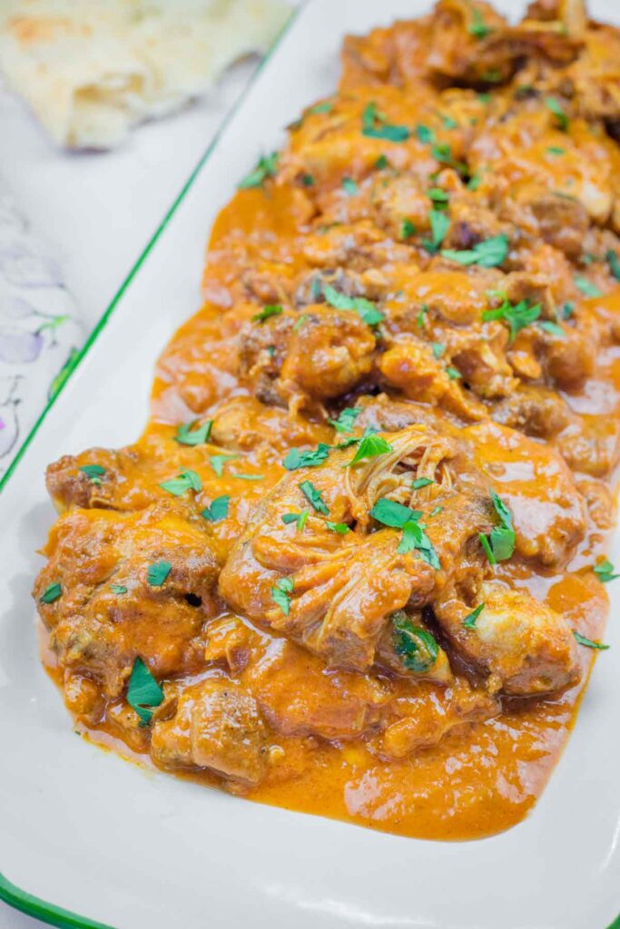 A rectangular plate filled with chicken pieces in an orange curry sauce, garnished with chopped green herbs.