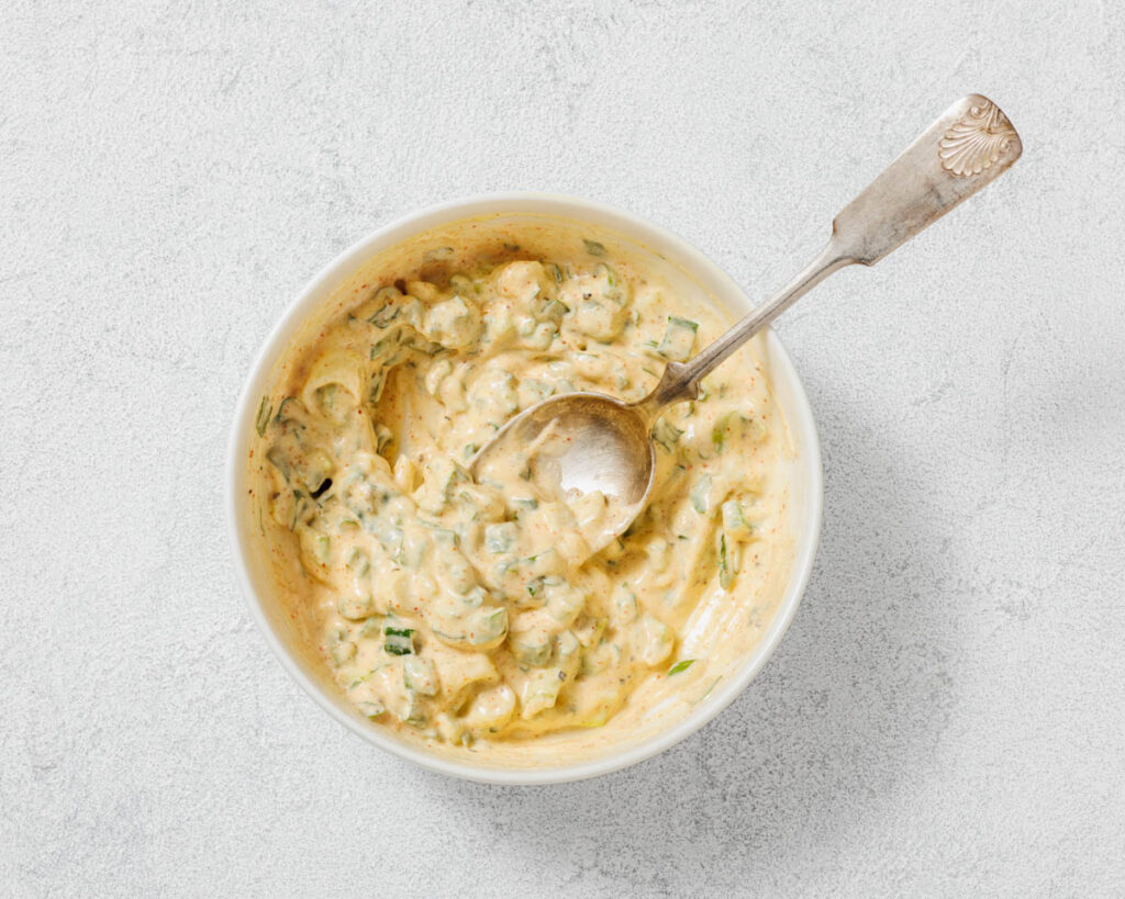 Overhead shot of a creamy sauce in a white bowl with a silver spoon.