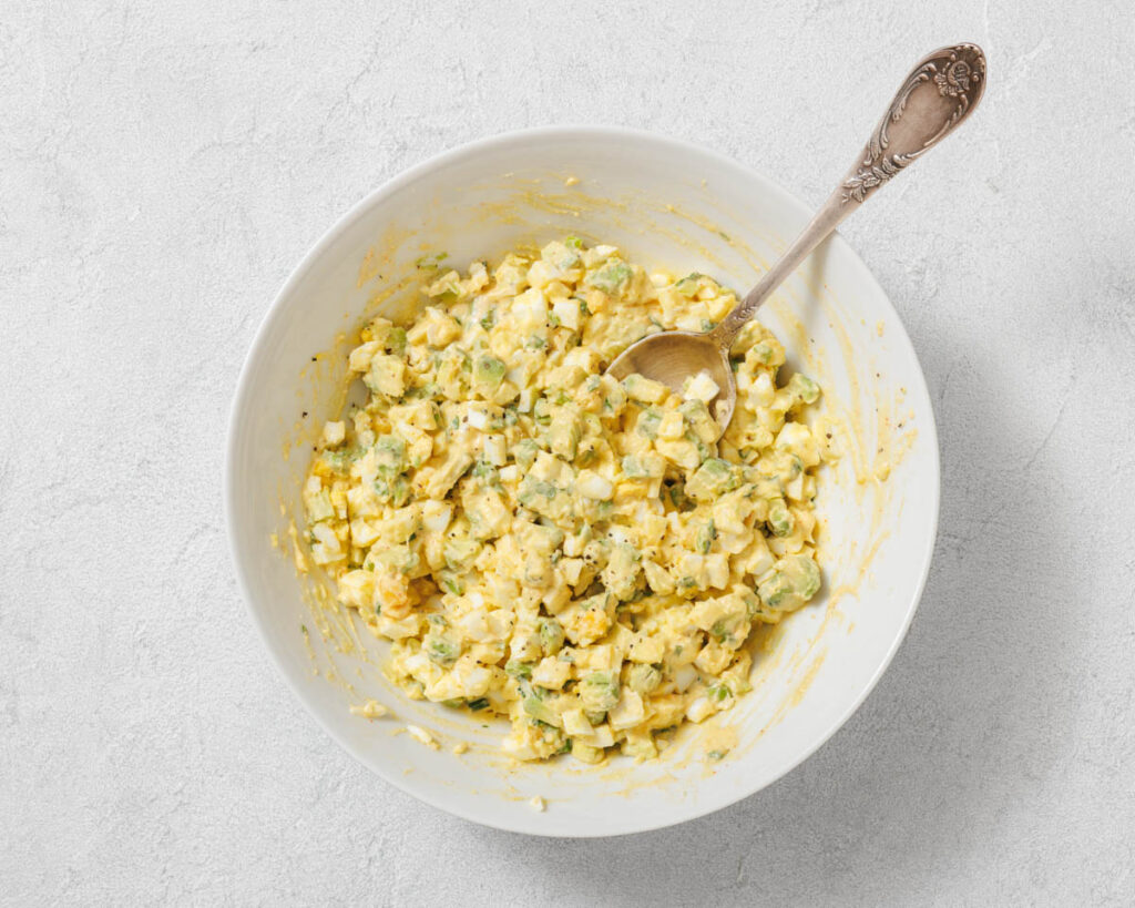 Overhead shot of avocado egg salad in a white bowl with a silver spoon.