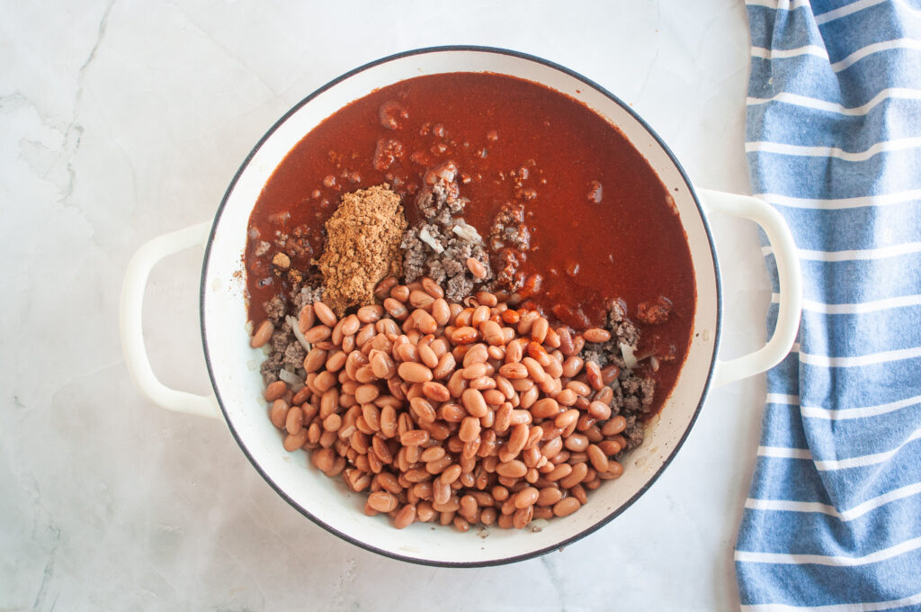 Overhead shot of cooked ground beef, onions, spices, chili sauce, and beans in a white pot.