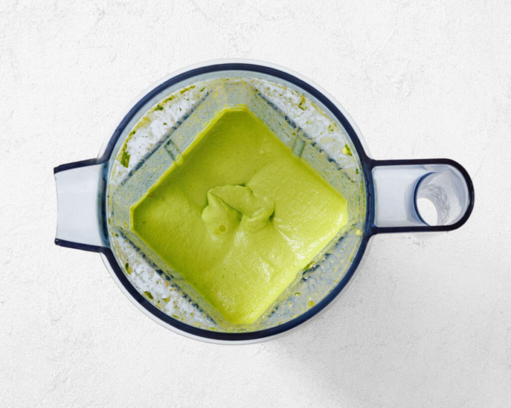 A blender filled with smooth green avocado puree, viewed from above on a light-colored surface.