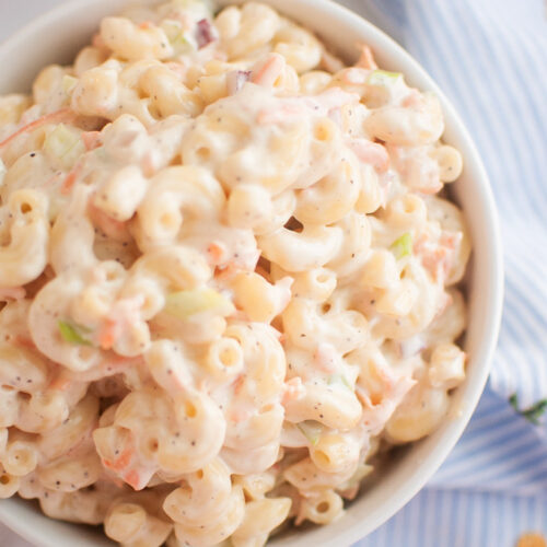 A white bowl filled with macaroni salad, containing elbow macaroni and a creamy dressing, is shown from an overhead angle.
