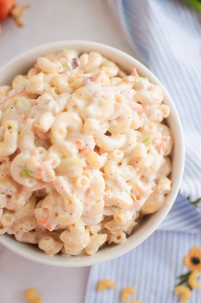 A white bowl filled with macaroni salad, containing elbow macaroni and a creamy dressing, is shown from an overhead angle.