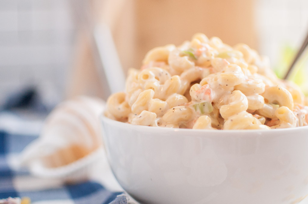 A close-up shot of a white bowl filled with macaroni salad, containing elbow macaroni and a creamy dressing.