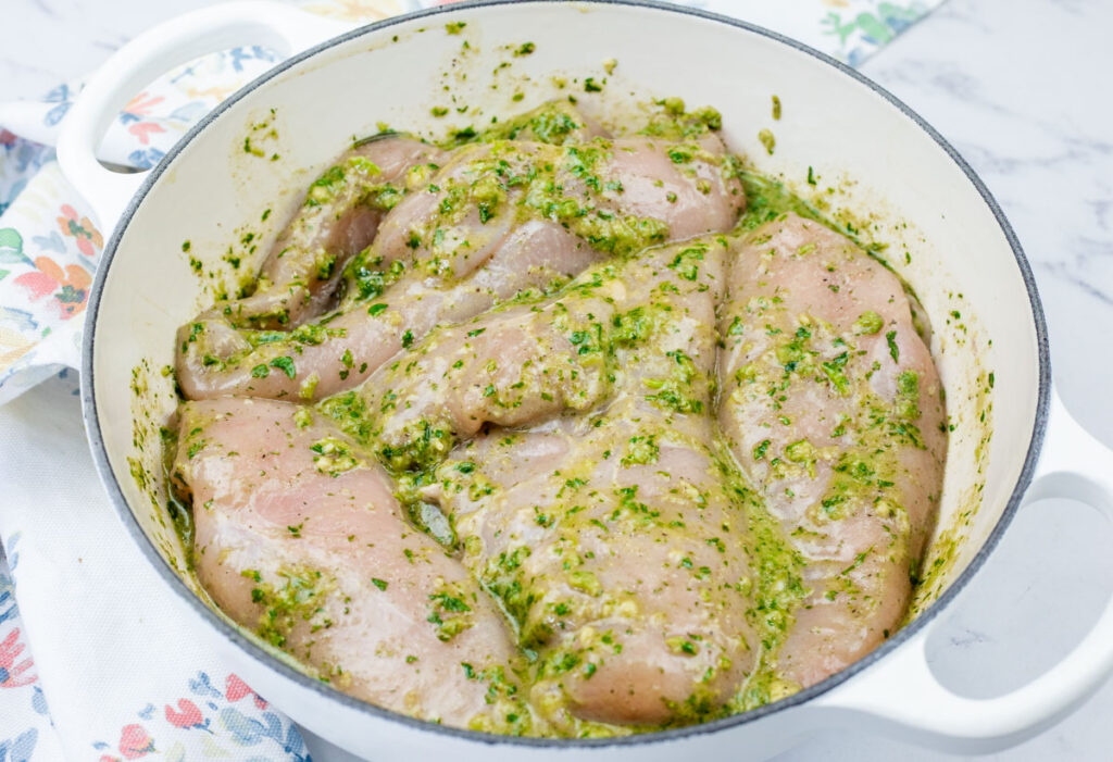 Raw chicken breasts coated with herbs seasonings in a white bowl.