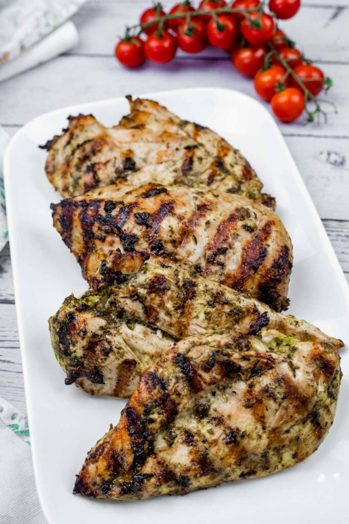 Grilled chicken on white plate with tomatoes in the background