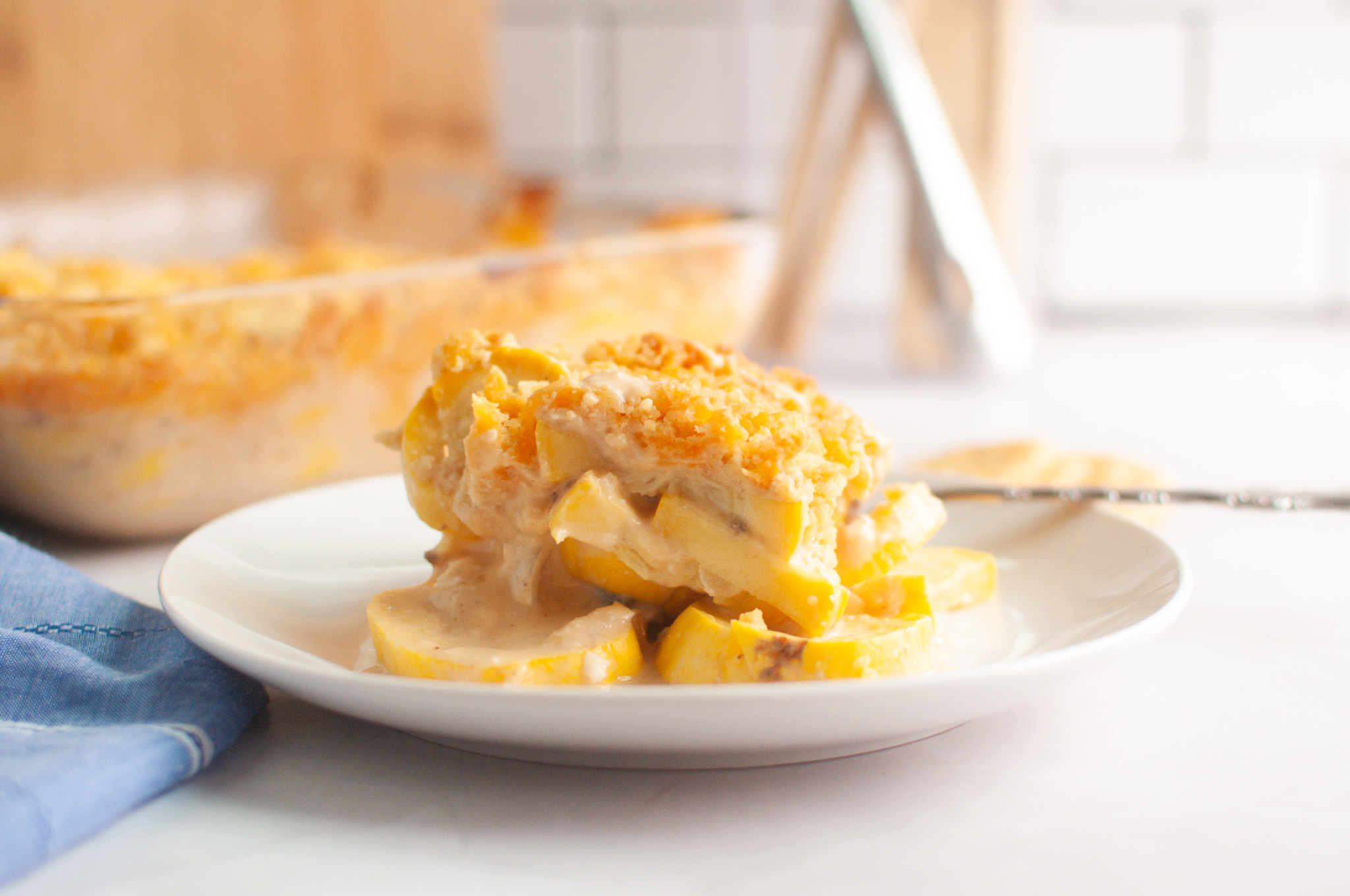 A serving of squash casserole with a crumb topping is plated on a white dish.
