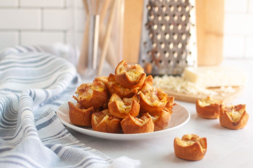 A white plate piled with small, golden-brown ham and cheese puffs.