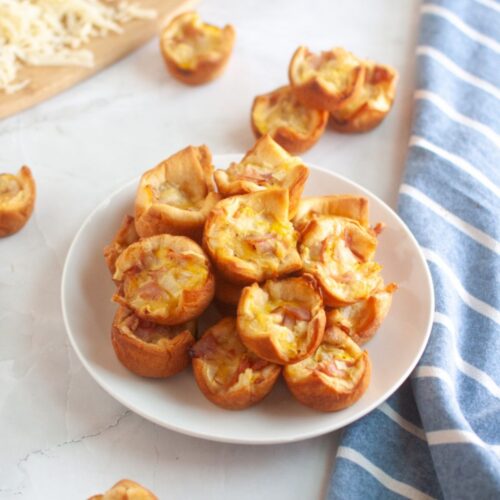 A white plate piled with small, golden-brown ham and cheese puffs.
