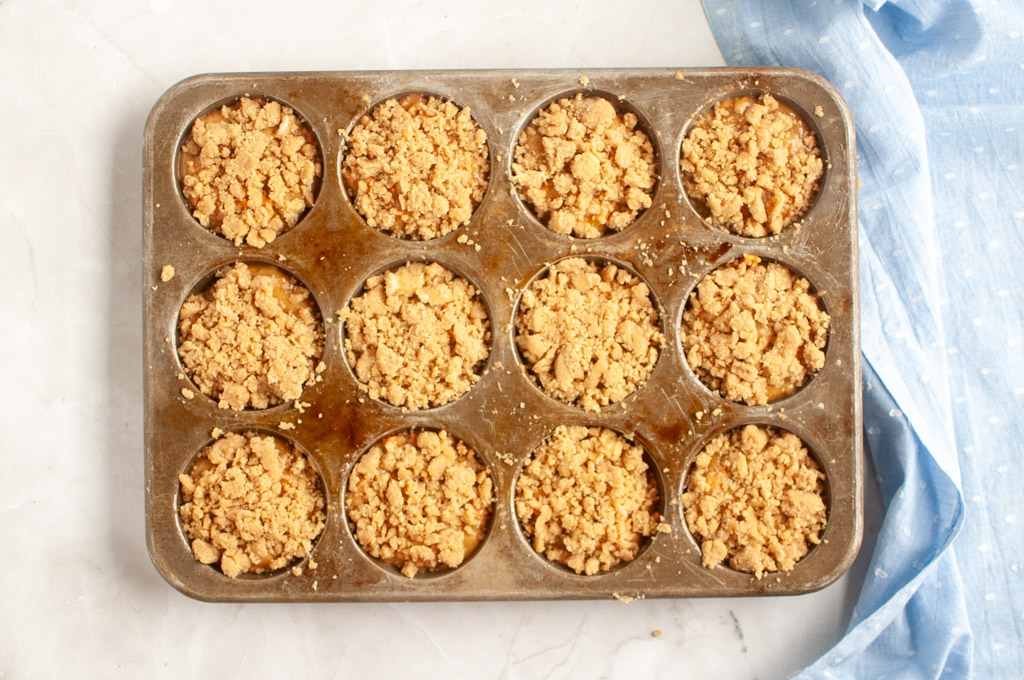 Overhead shot of a carrot muffin tin filled with apple muffin batter and topped with crumble.