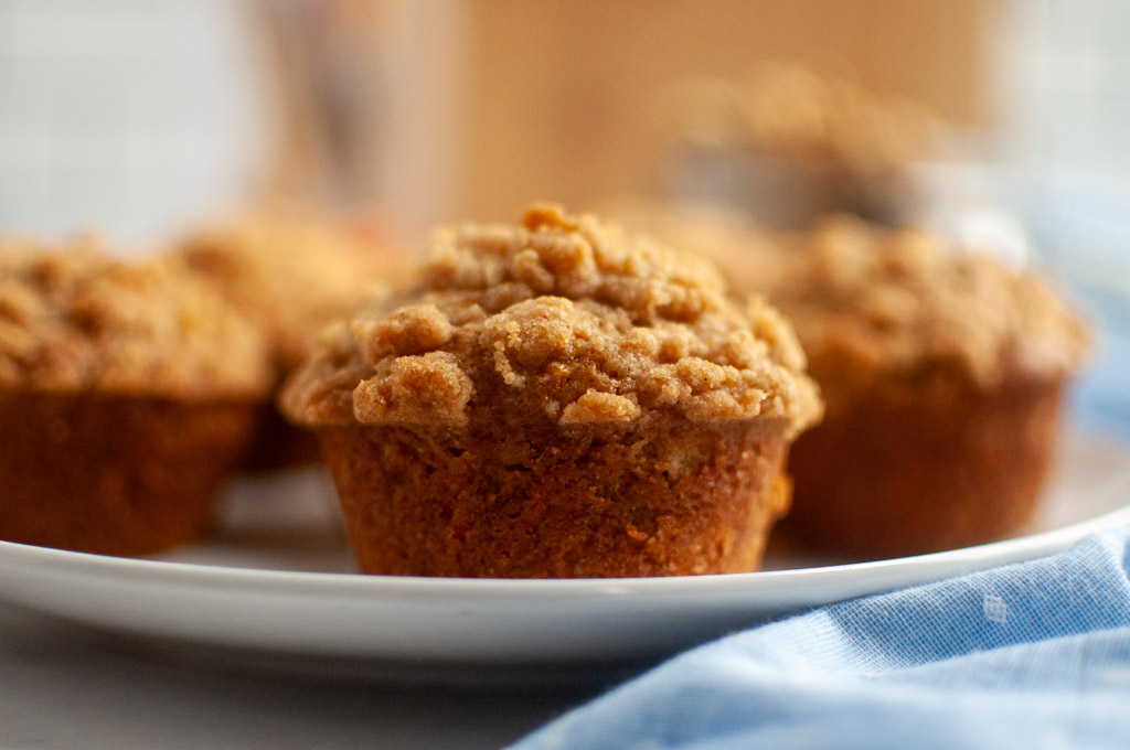Several golden-brown carrot muffins with a crumbly topping on a white plate.