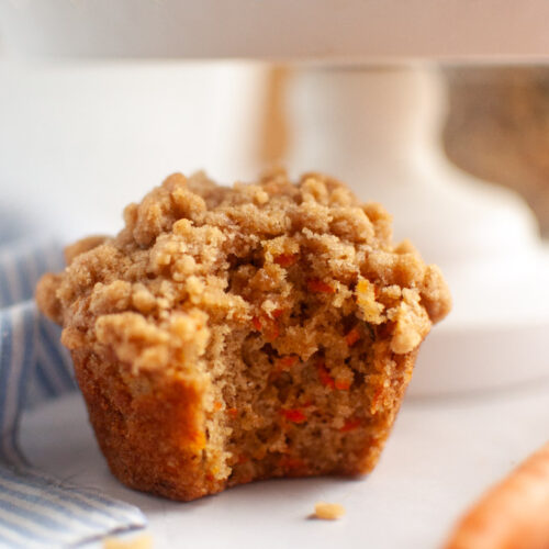 A close-up of a carrot oat muffin with a crumbly topping, with a bite missing.