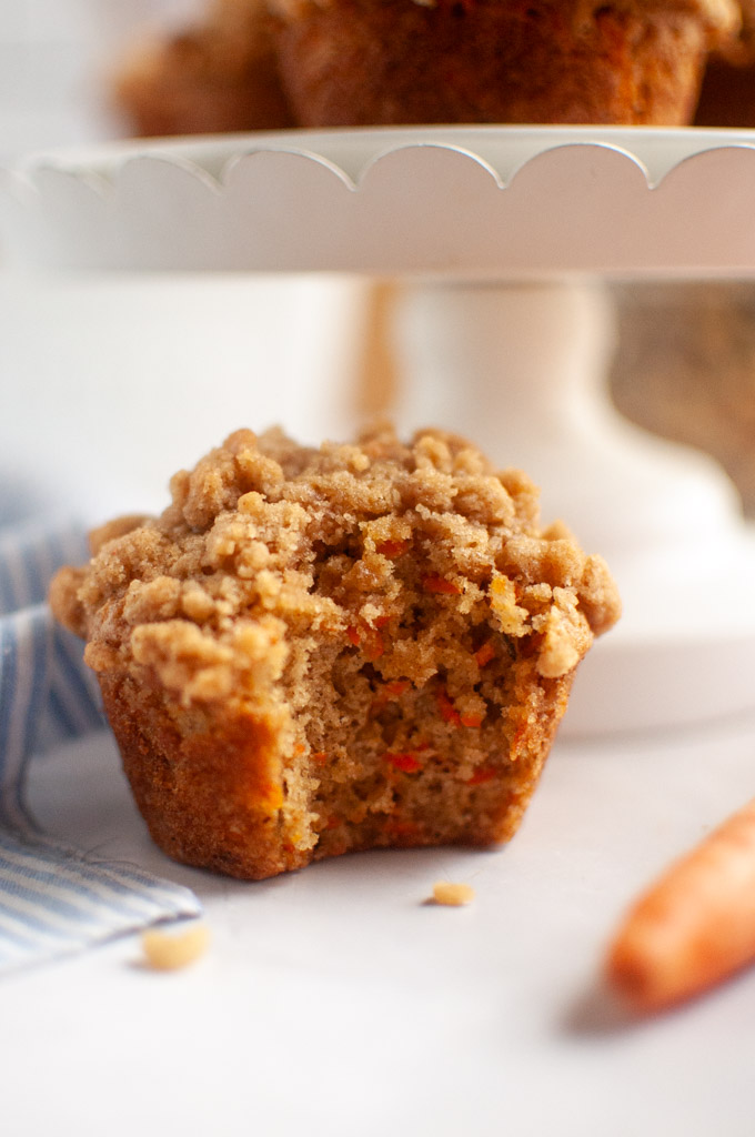 A close-up of a carrot oat muffin with a crumbly topping, with a bite missing.