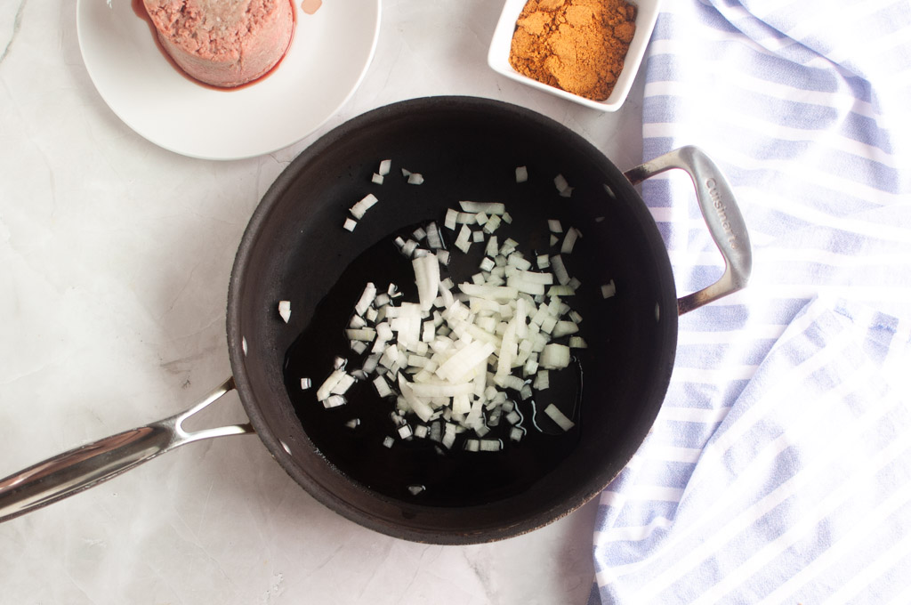 Overhead shot of diced white onions sautéing in oil in a black skillet.