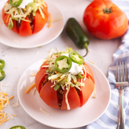 A ripe red tomato, hollowed out and filled with taco meat and toppings, on a white plate.