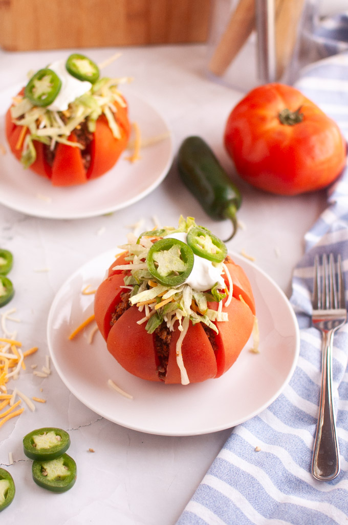 A ripe red tomato, hollowed out and filled with taco meat and toppings, on a white plate.