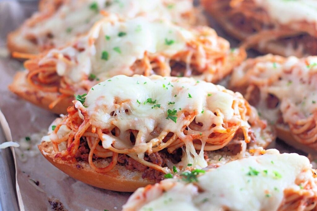 Toasted bread halves topped with spaghetti, meat sauce, and melted cheese, garnished with chopped parsley.