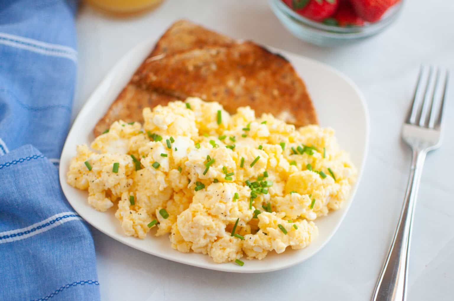 A plate of scrambled eggs garnished with chives, served with two slices of toast.