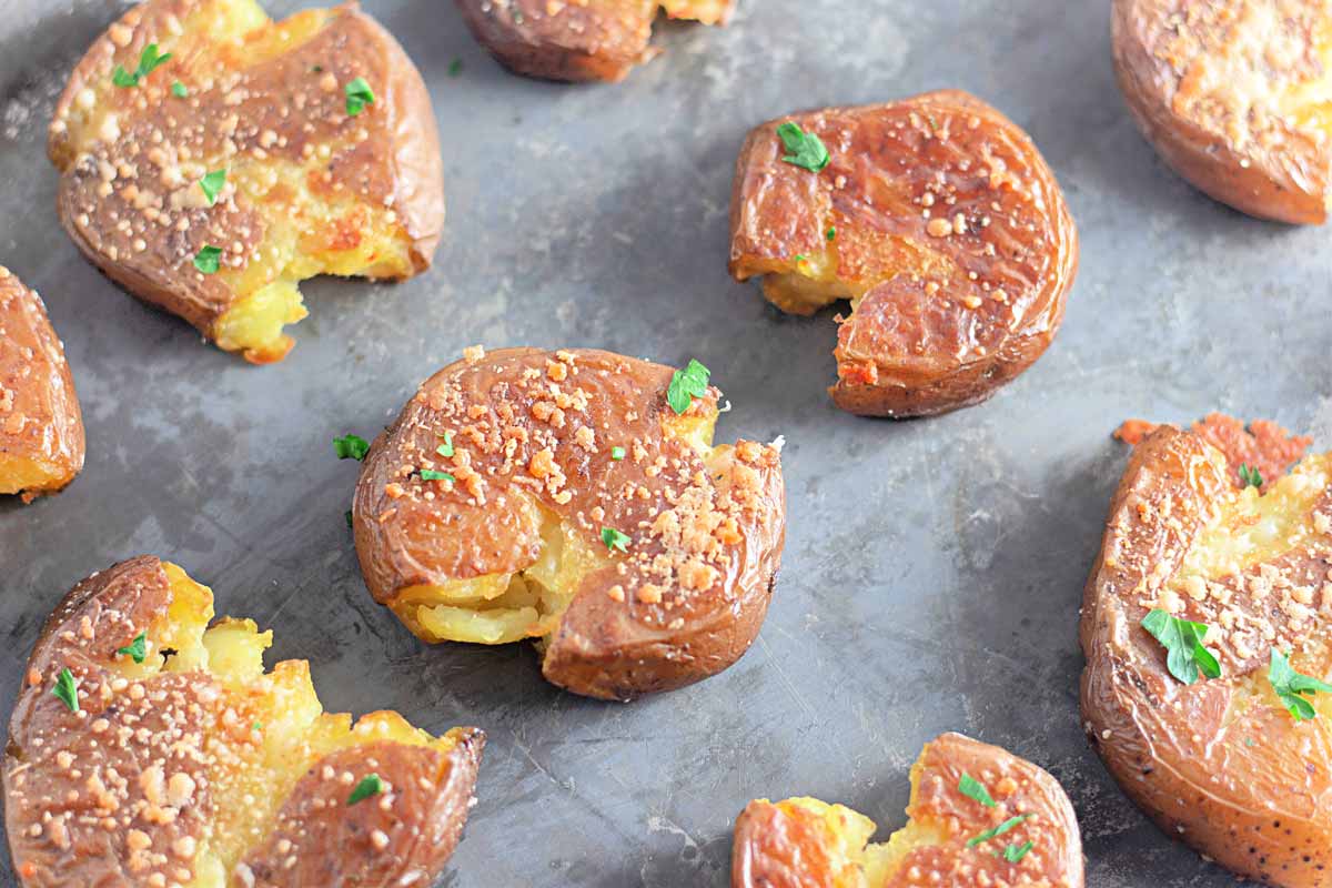 Crispy Garlic Parmesan Smashed Potatoes topped with herbs and grated cheese on a metal baking sheet.