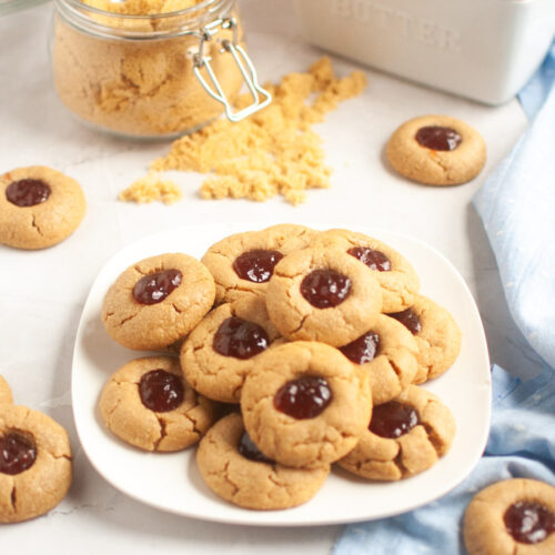 A white plate filled with golden-brown peanut butter cookies with a dollop of red jelly in the center of each.
