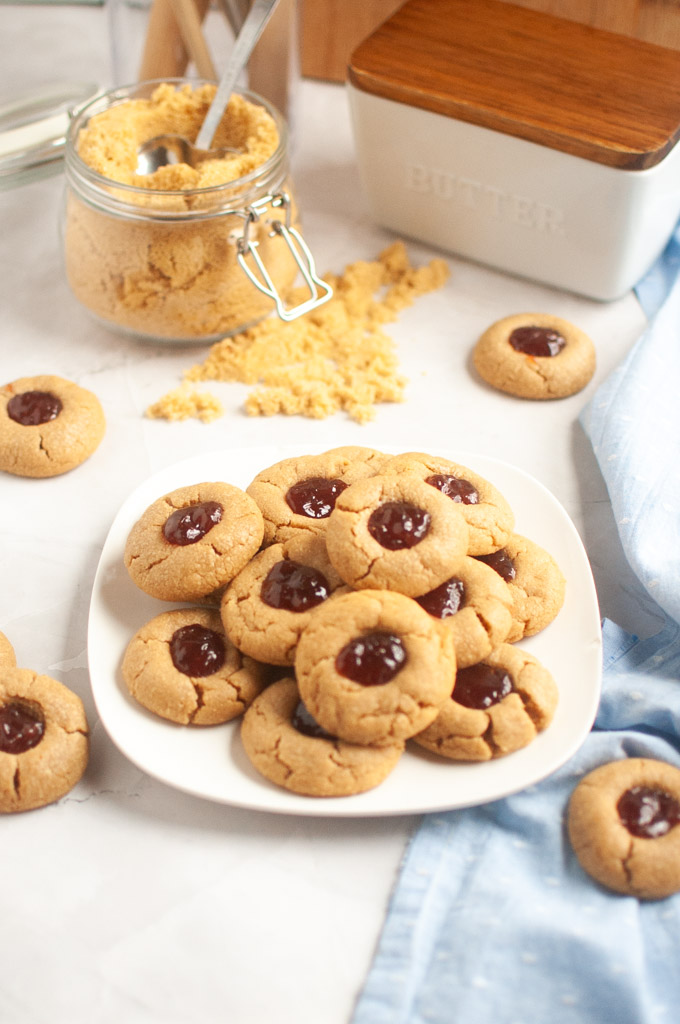 A white plate filled with golden-brown peanut butter cookies with a dollop of red jelly in the center of each.