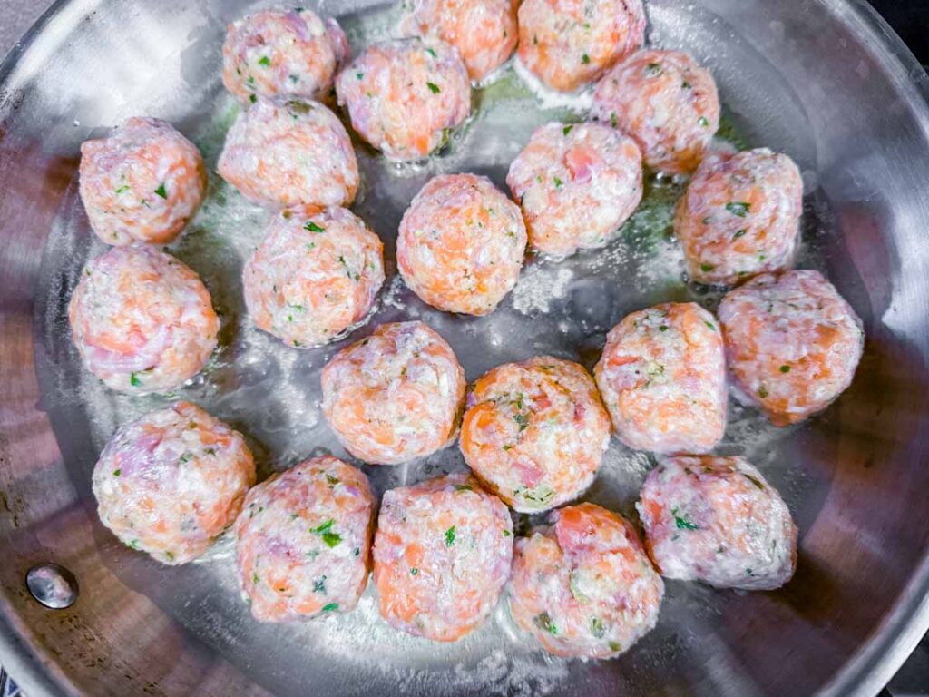Overhead shot of raw salmon balls cooking in a pan.