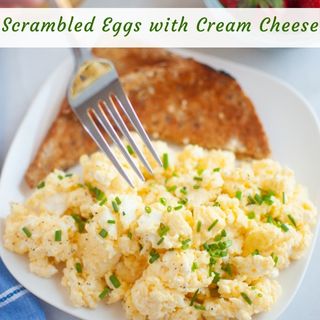 A plate of scrambled eggs with cream cheese, garnished with chopped chives, and served with two slices of toasted bread.