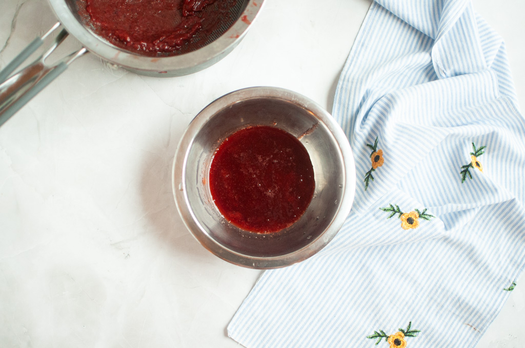 Overhead shot of a metal bowl containing smooth, dark red strained strawberry jam.