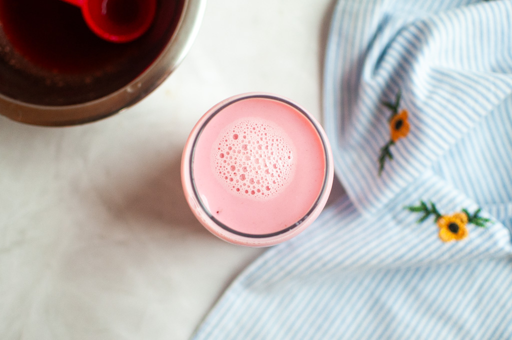 Overhead shot of a glass filled with a pink strawberry milk with bubbles on top.