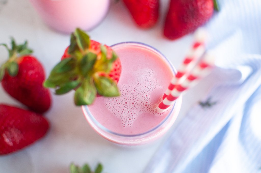 Overhead shot of a glass filled with a pink strawberry milk, garnished with a strawberry and two red and white straws.