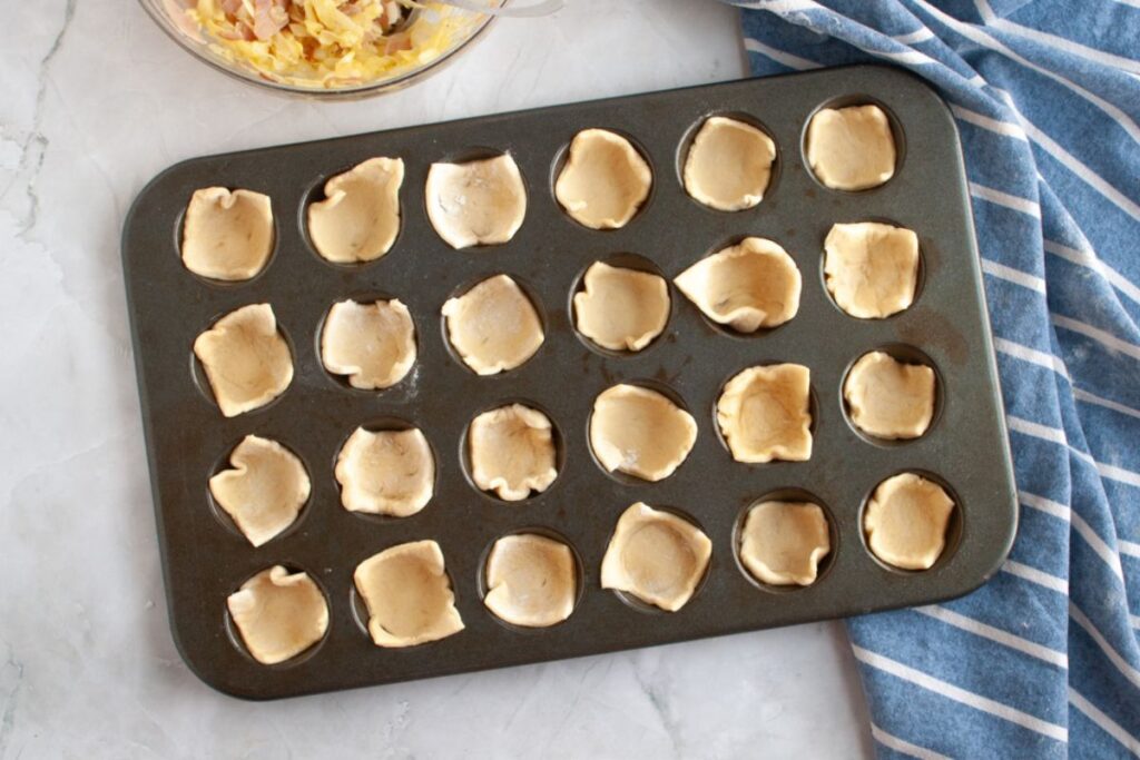 Overhead shot of a muffin tin lined with small pieces of dough, ready for filling.
