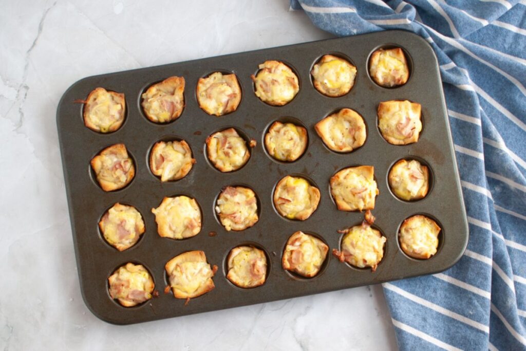 Overhead shot of a muffin tin filled with small, golden-brown ham & cheese puffs.