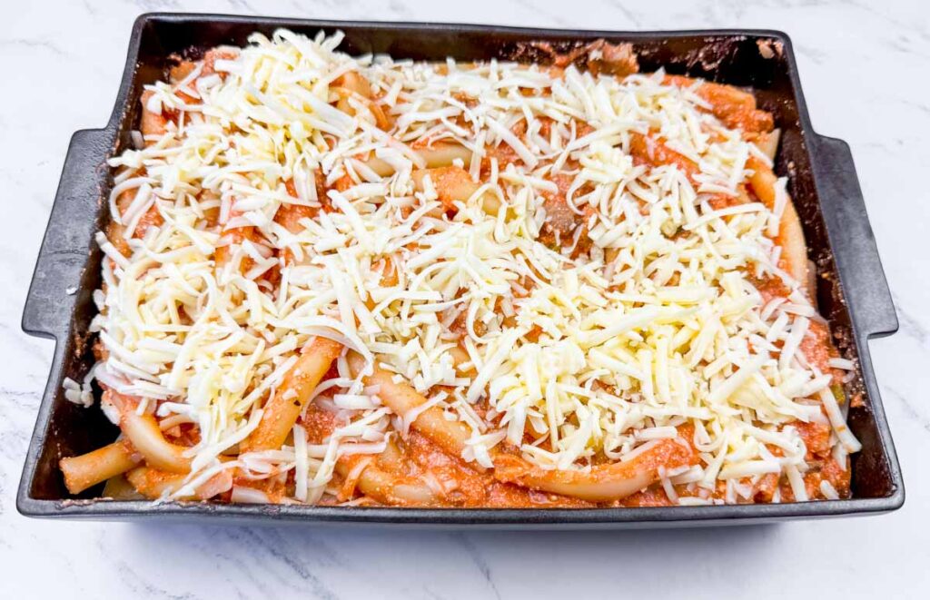 Adding cheese toppings on Classic Baked Ziti.