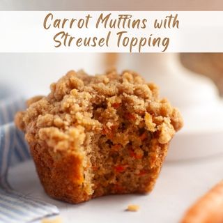 A carrot muffin with streusel topping sits on a surface, with a bite taken out, showing the moist interior and visible carrot pieces.