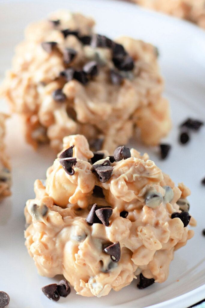 Close-up of a no-bake cookie cluster made with cereal, white coating, and mini chocolate chips, placed on a white plate.