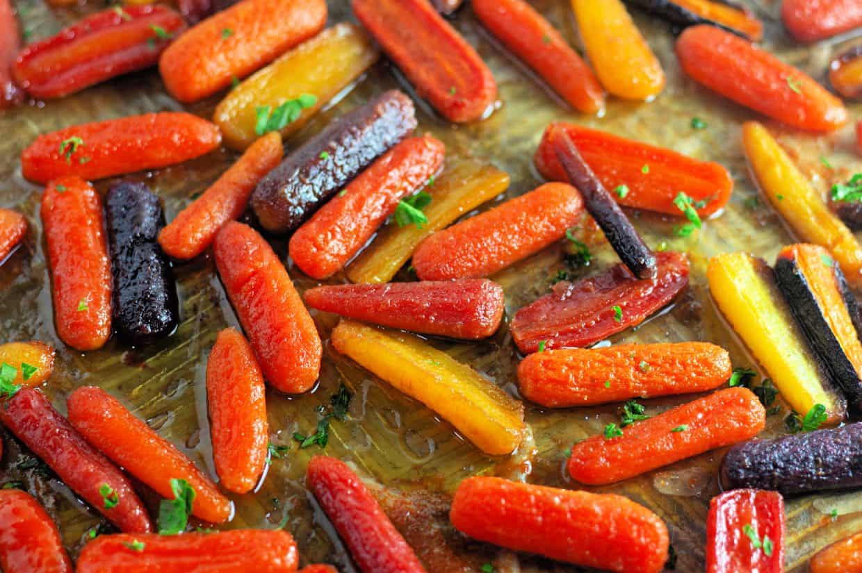 Assorted roasted baby carrots in orange, yellow, and purple colors on a baking sheet, garnished with chopped herbs.