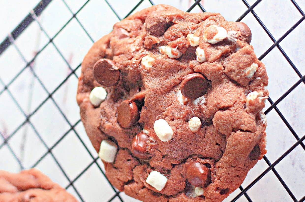 A close-up of a cocoa chip cookie with white and dark chocolate chunks resting on a black cooling rack.
