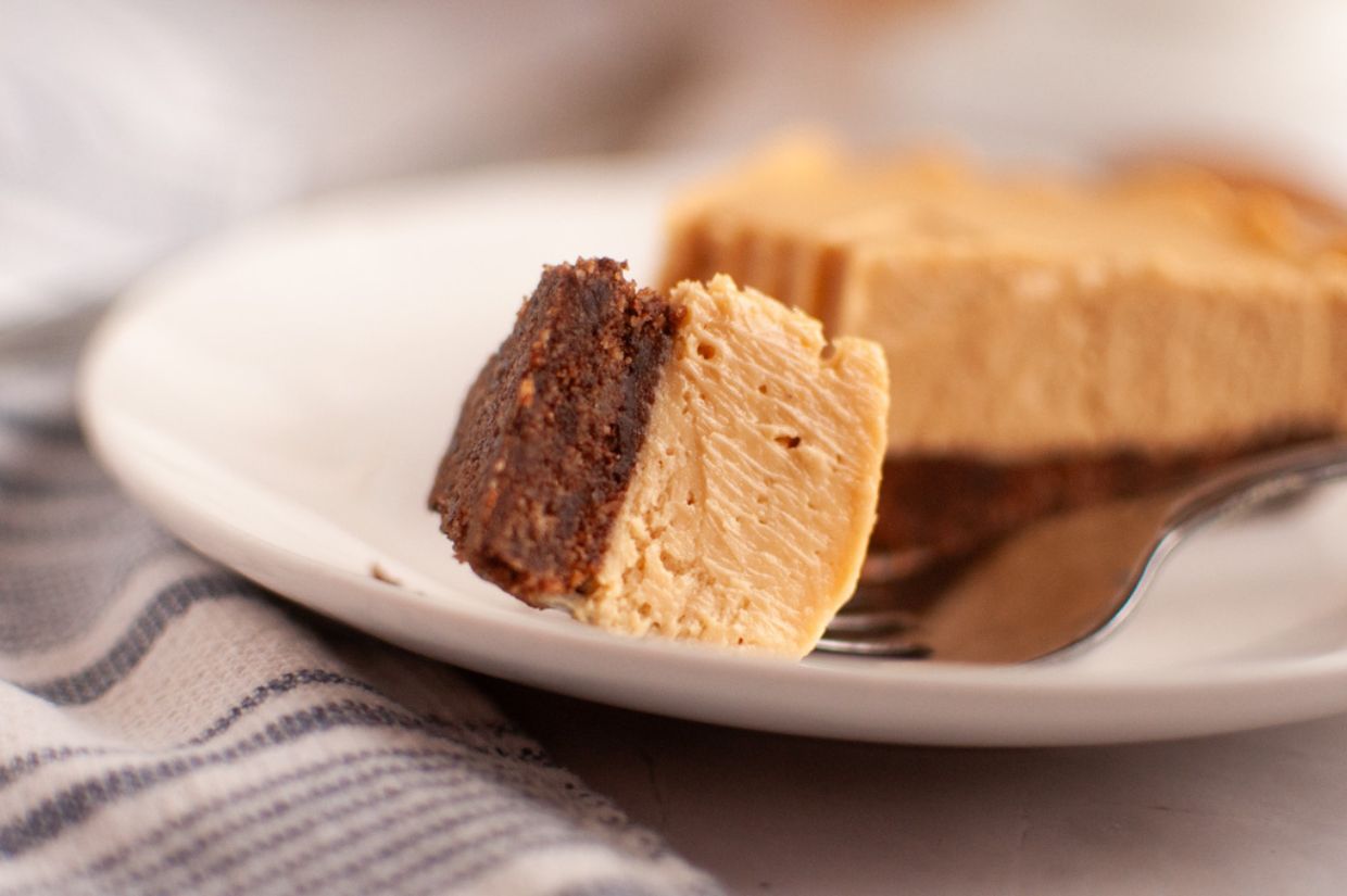 A fork holds a bite of creamy pie with a brown crust, resting on a white plate with a blurred background.