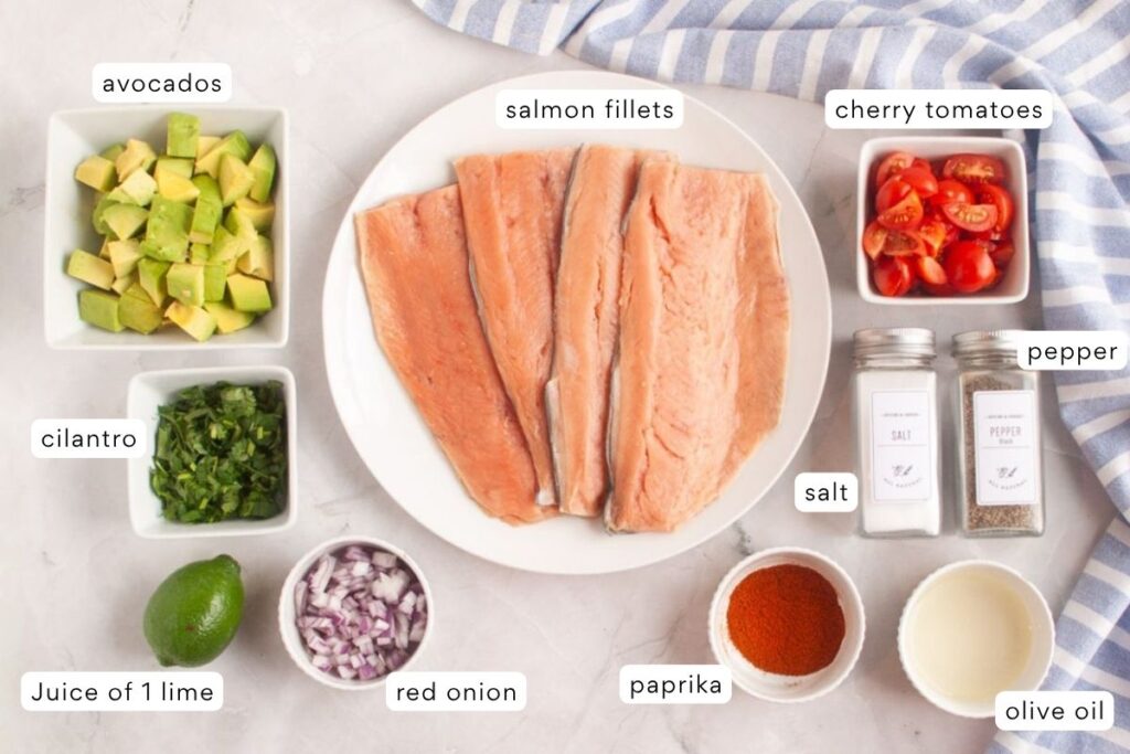 Overhead view of salmon fillets on a plate surrounded by bowls of diced avocado, cherry tomatoes, cilantro, red onion, lime juice, paprika, olive oil, salt, and pepper.