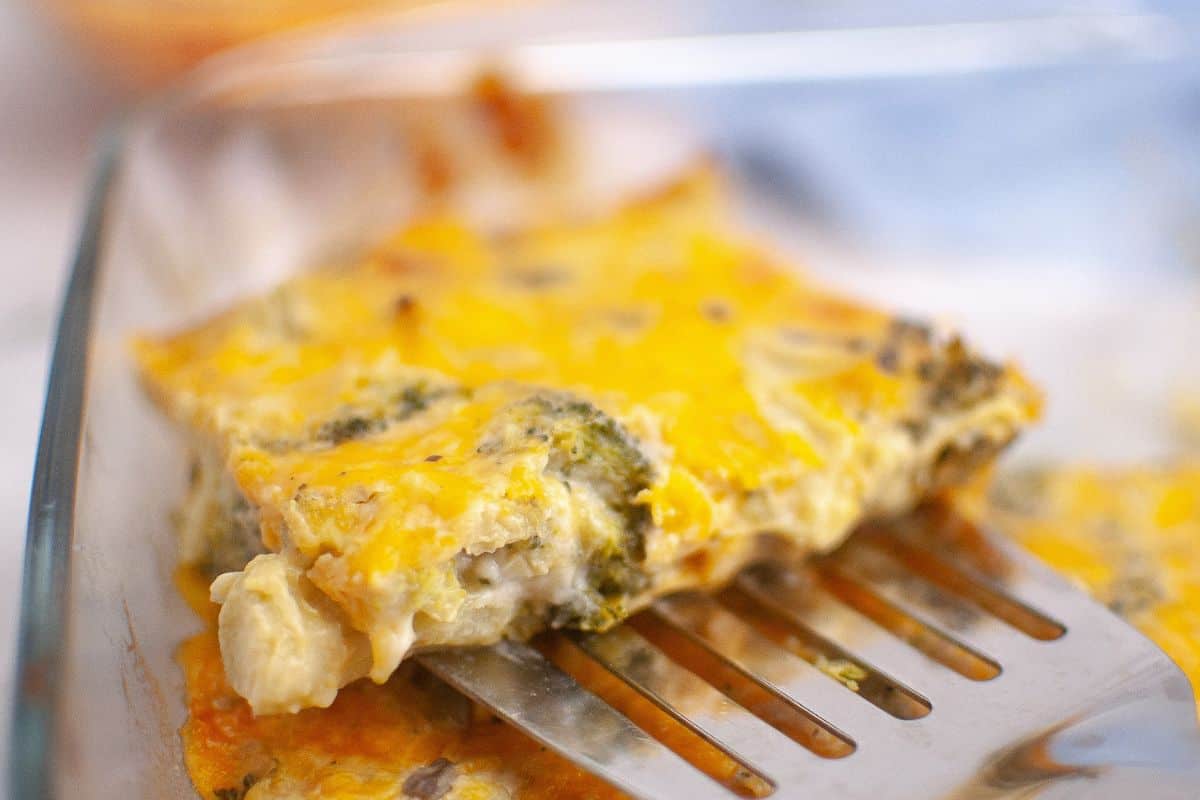 A metal spatula lifts a slice of 3-Ingredient Broccoli Cheese Casserole from a glass baking dish.