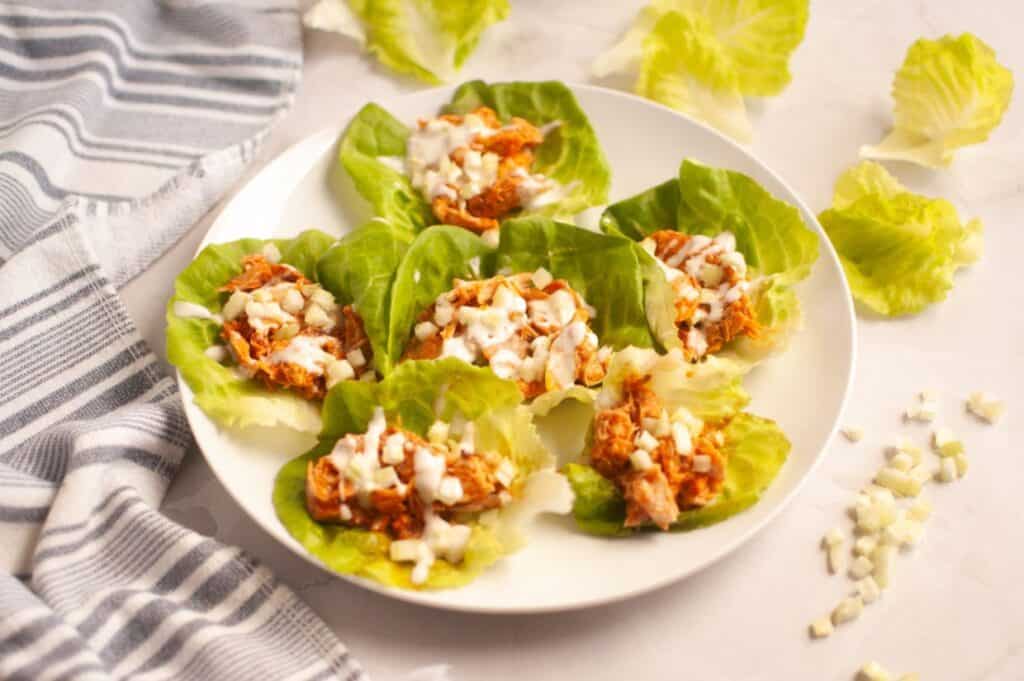A white plate with six Buffalo Chicken Lettuce Wraps placed next to a striped towel.