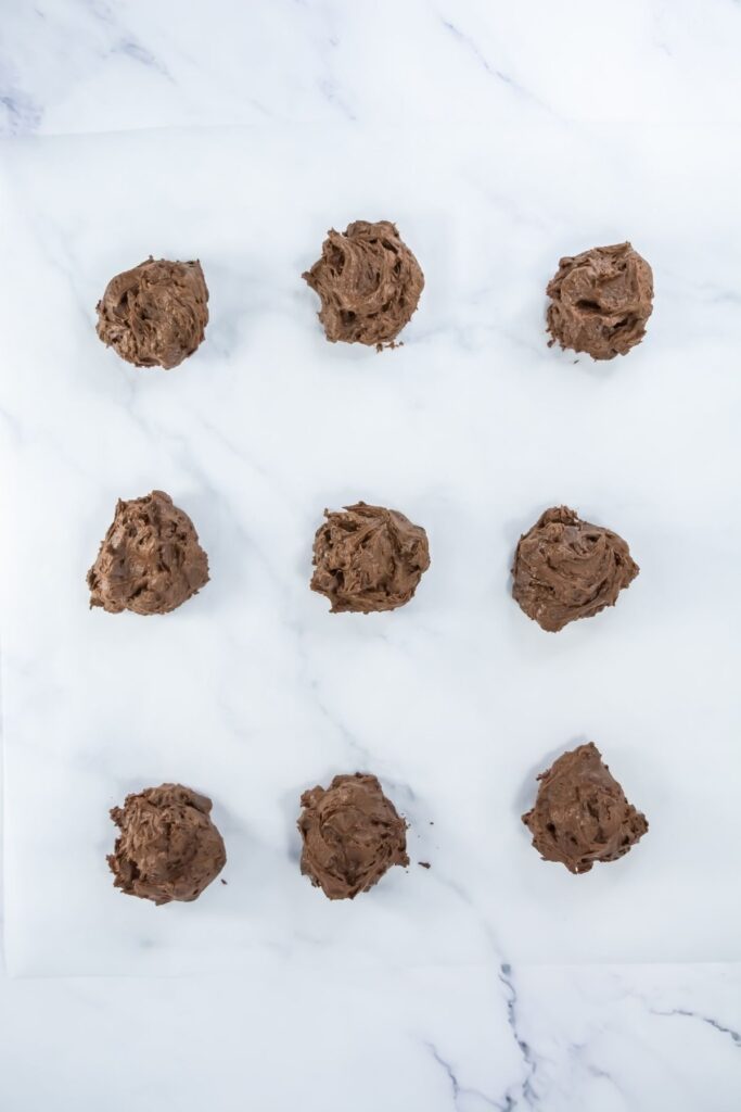 Nine scoops of chocolate cookie dough are arranged in three rows on a white marble surface.