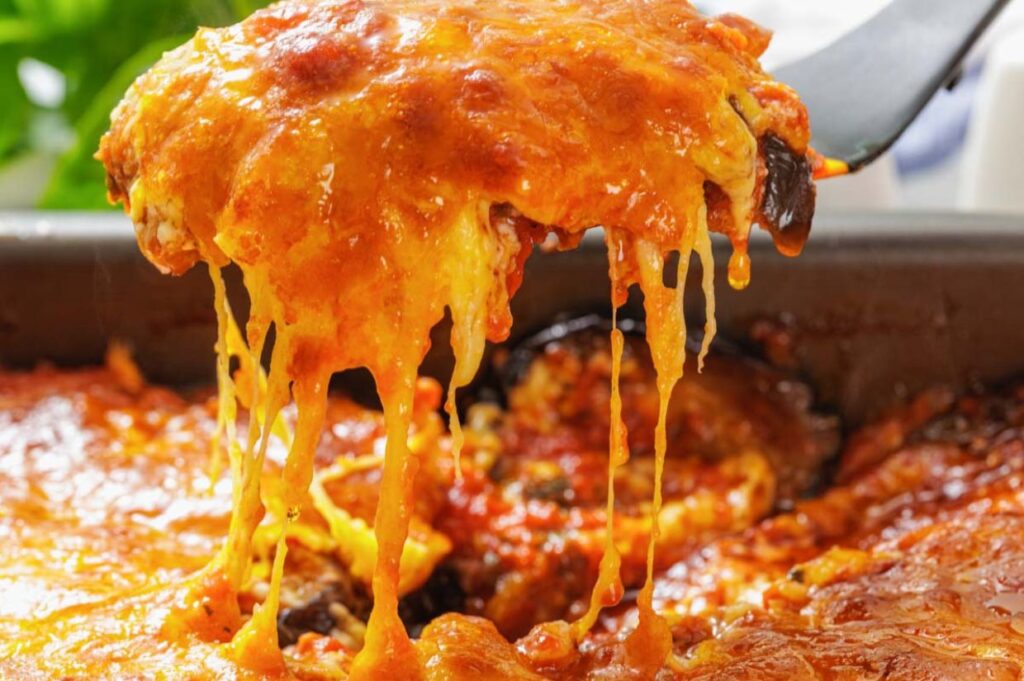 A serving of cheesy baked casserole being lifted from a pan, with melted cheese stretching.