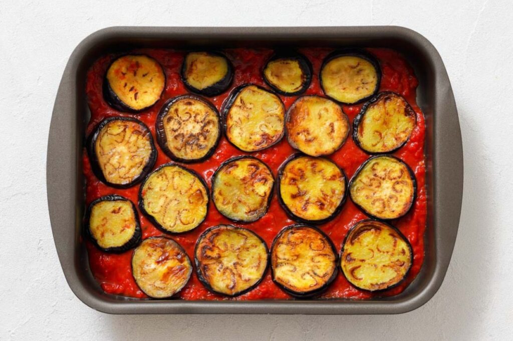 A baking dish filled with a layer of roasted eggplant slices on top of red tomato sauce.
