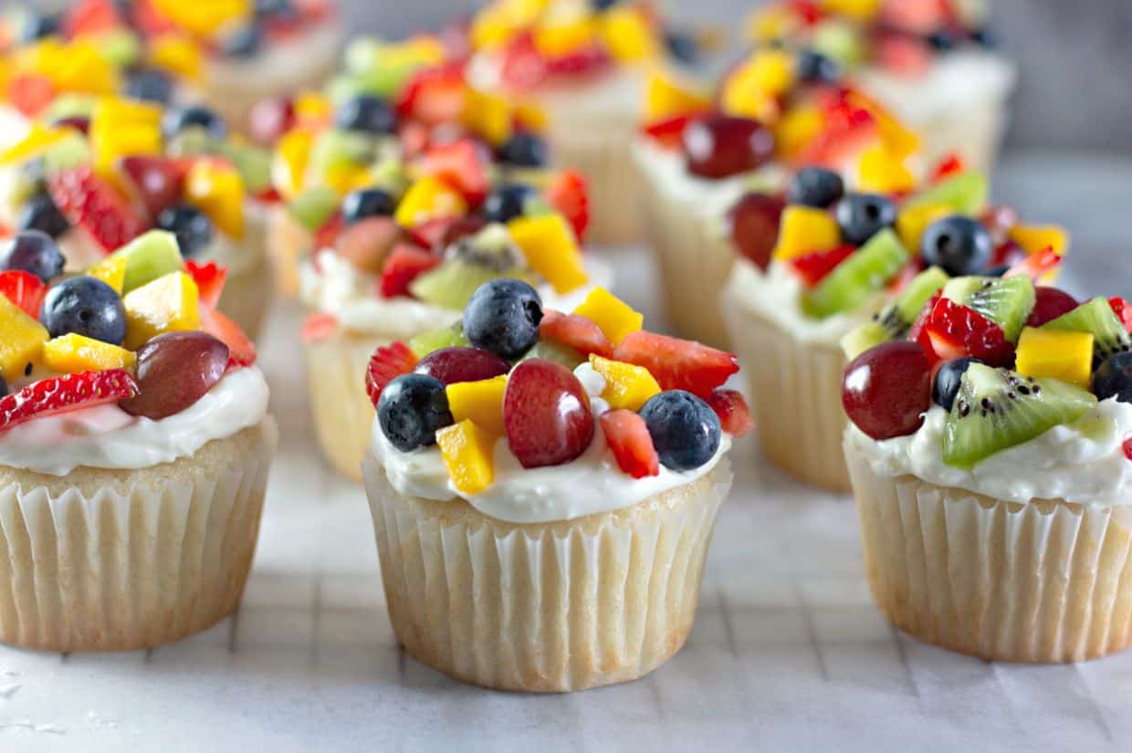 A close-up, eye-level view of several mini fruit pizza cupcakes on a white surface.