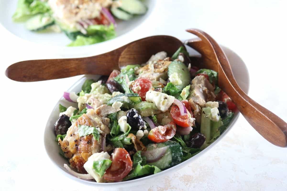 Oval bowl filled with Chicken Mediterranean Salad Recipe with wooden salad servers on the side.